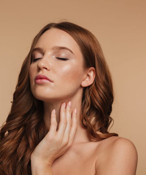 Beauty portrait of sensual ginger woman with long hair posing with closed eyes over cream background