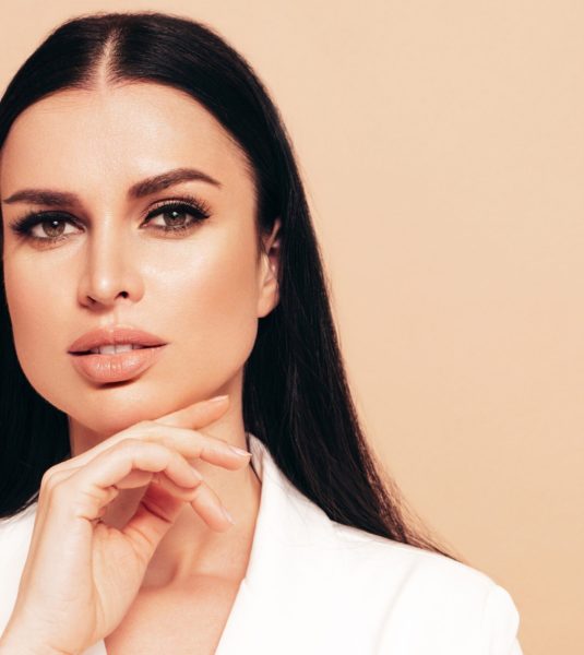 High fashion portrait of young beautiful brunette woman wearing nice trendy white suit. Sexy fashion model posing in studio. Fashionable female isolated on beige